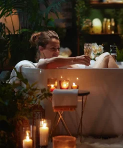 Kobieta relaksująca się w wannie przy świecach, tworząca wieczorny rytuał z aromatyczną solą Czterech Alchemików.