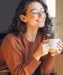 Kobieta z uśmiechem trzyma ciepły kubek - herbata K. HEBDA, w nastrojowym, domowym świetle.