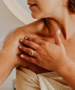 Kobieca dłoń nakłada masło DobraNocka na skórę ramienia, tworząc zmysłowy, wieczorny rytuał pielęgnacyjny.