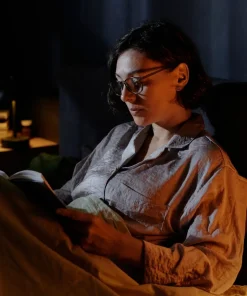 Herbatka Na dobry sen Klaudyna Hebda towarzyszy wieczornej chwili wyciszenia kobiety czytającej książkę w ciepłym świetle.