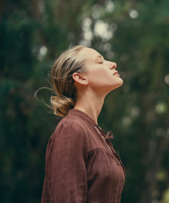 Kobieta z zamkniętymi oczami wśród drzew – aromaterapia i odprężenie z olejkiem Chatka w lesie K. HEBDA