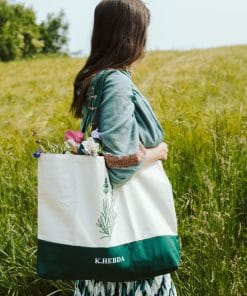 Kobieta w zielonej sukience z dużą torbą bawełnianą Klaudyna Hebda i bukietem kwiatów na łące