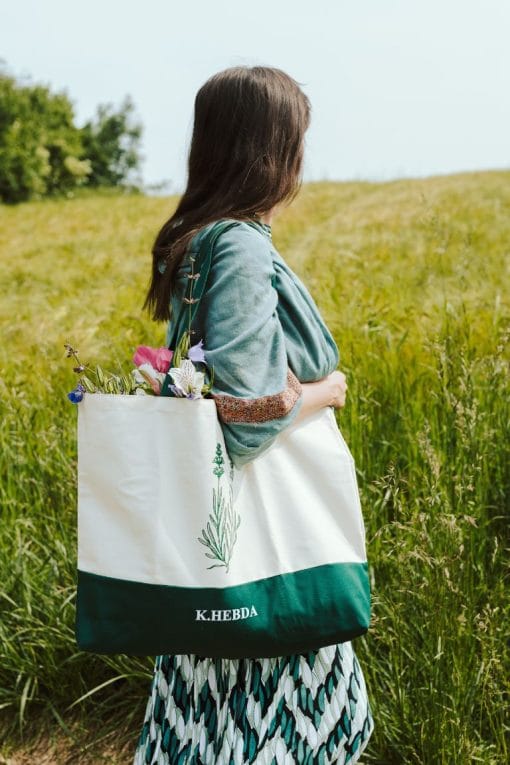 Kobieta w zielonej sukience z dużą torbą bawełnianą Klaudyna Hebda i bukietem kwiatów na łące
