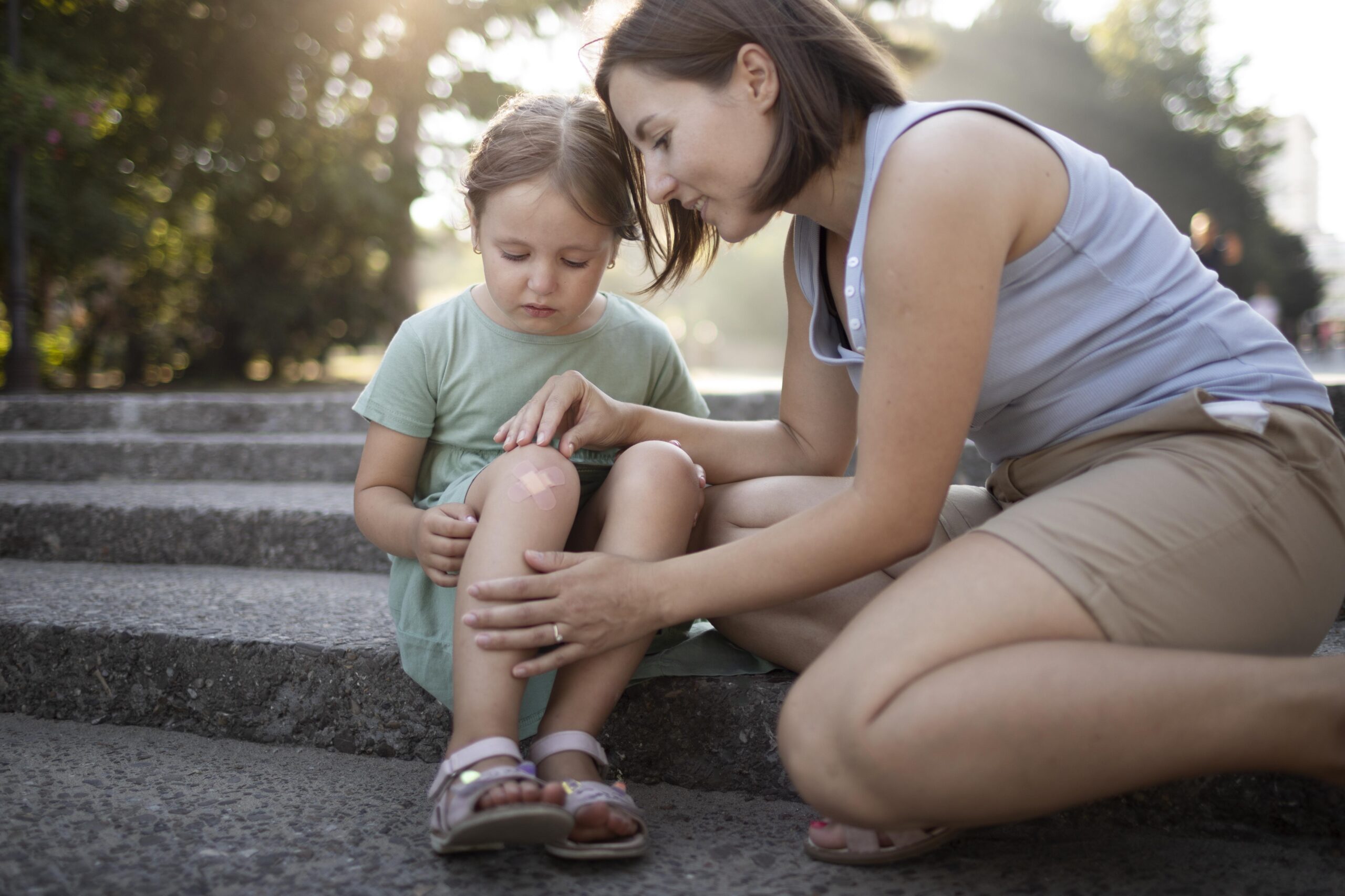Mama troskliwie oglądająca kolano dziecka po zabawie na świeżym powietrzu – zdjęcie symbolizujące zastosowanie maści arnikowej dla aktywnych i małych odkrywców.