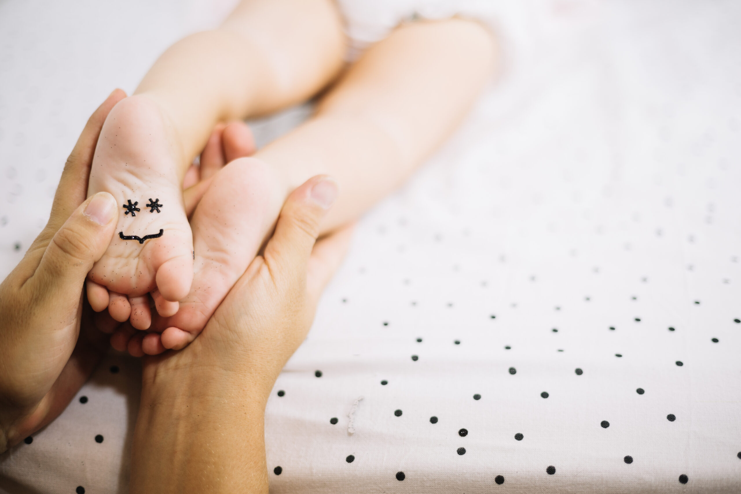 Mama wykonująca delikatny masaż stóp dziecka z użyciem oliwy magnezowej K. Hebda podczas wieczornej pielęgnacji.