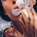Zmysłowe zbliżenie na usta kobiety trzymającej biały kwiat frangipani, symbolizujący niszowy zapach Flower Paradox.