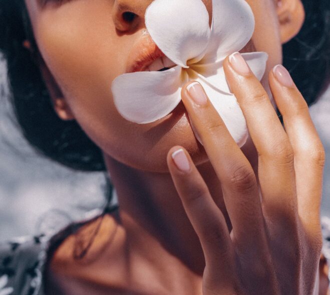 Zmysłowe zbliżenie na usta kobiety trzymającej biały kwiat frangipani, symbolizujący niszowy zapach Flower Paradox.