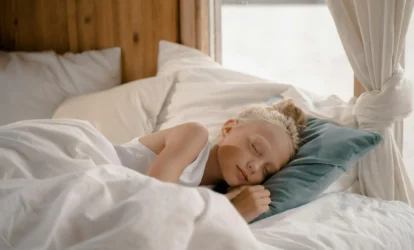 Dziewczynka z blond włosami śpiąca w jasnej pościeli na szarej poduszce