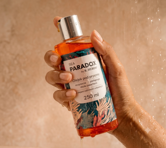 Butelka olejku pod prysznic Sea Paradox 250 ml w dłoni na tle kafelków i spływającej wody.
