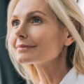Profil uśmiechniętej kobiety o jasnych włosach i gładkiej, wypoczętej cerze, prezentującej efekty działania regenerującego serum Blue Tansy + Vitamin C.