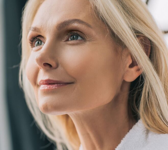 Profil uśmiechniętej kobiety o jasnych włosach i gładkiej, wypoczętej cerze, prezentującej efekty działania regenerującego serum Blue Tansy + Vitamin C.