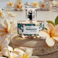 Flakon perfum damskich Flower Paradox by K. Hebda 50 ml na jasnym kamieniu w otoczeniu kwitnących, kremowych kwiatów.