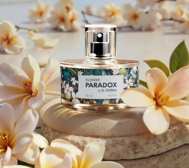 Flakon perfum damskich Flower Paradox by K. Hebda 50 ml na jasnym kamieniu w otoczeniu kwitnących, kremowych kwiatów.